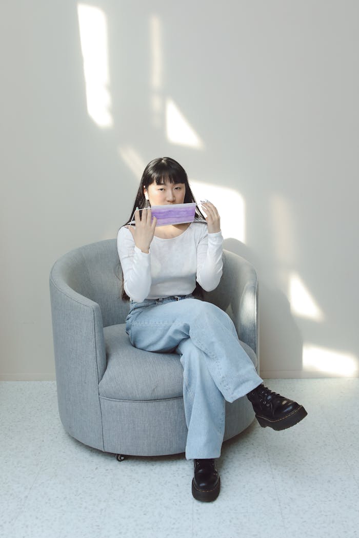 Fashionable woman sitting with mask on a modern chair, showcasing personal protection.